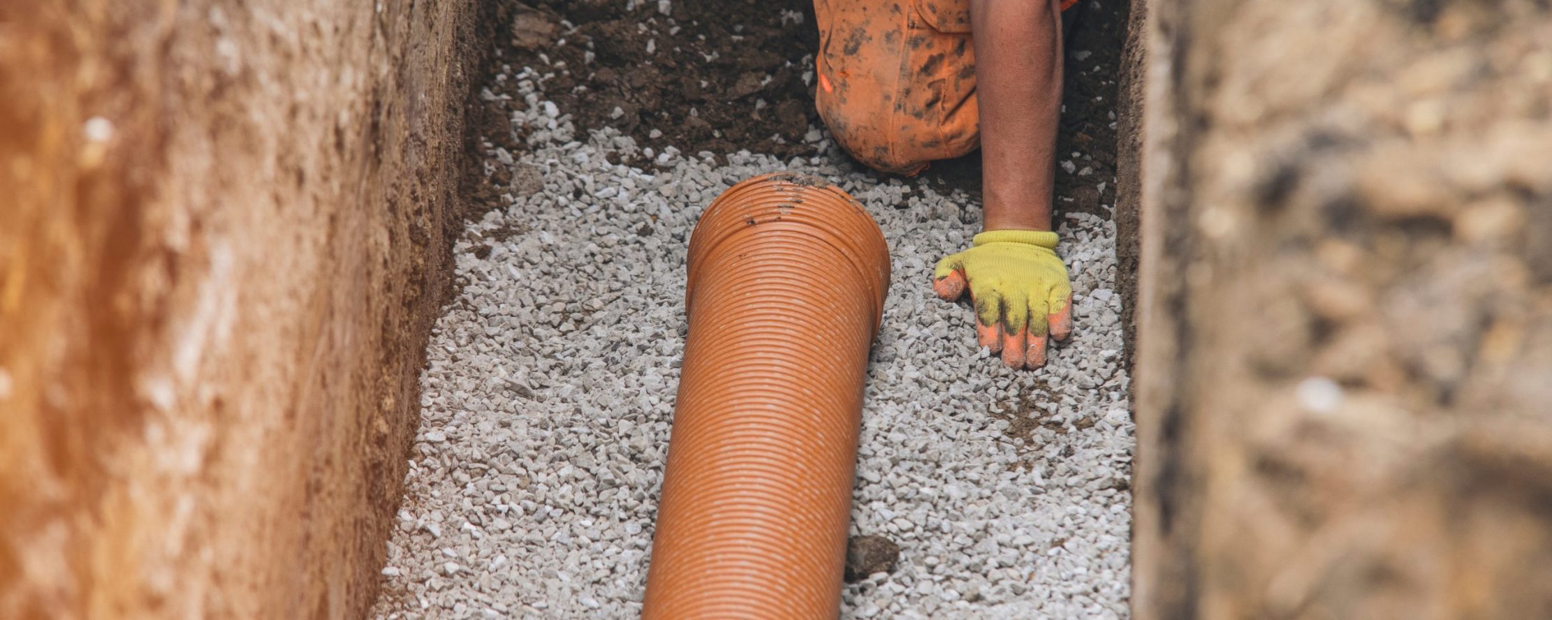 Worker,Installing,Drainage,Pipe,In,Trench,During,Construction